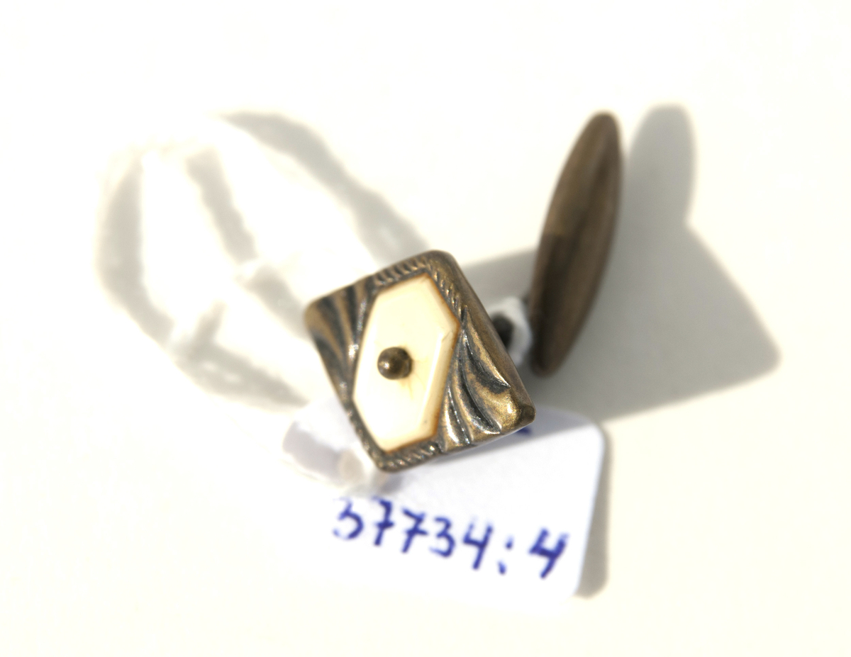 1:a Trekantig form, guldmetall, mönstrad med små linjer samt 1 liten pärla i mitten. Bygel fast i ena änden, andra rörlig del för iträdning i knapphålen.
2:a Oval form, mässingram, pärlemorbotten samt en romb i grönt i mitten. Bygel samma som ovan.
3:e Rund form, guldmetall, mönstrad i halvmåneform ytterkant på 2 sidor, raka streck på mitten och en liten cirkel i över och underkant med en ring runt om. Bygel samma som ovan.
4:e Rombform, mörk metall, mönster lite droppform, i mitten rektangel med spets i varje ände av pärlemor samt en liten metallkula i mitten. Bygel samma som ovan.