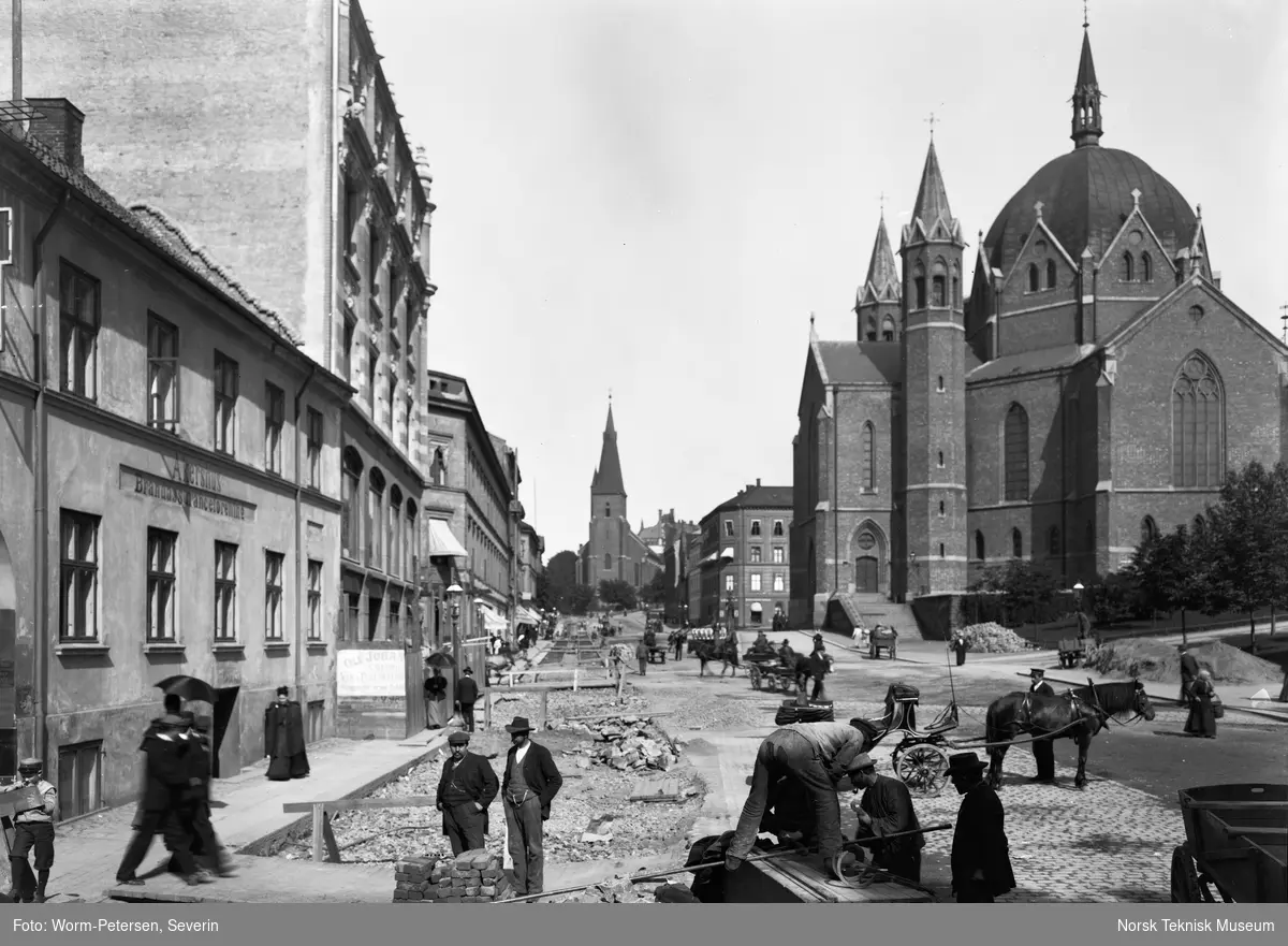 Legging av trikkeskinner i Akersgata i 1899. Bildet er tatt under arbeidet med ny sporvei fra Akersgata 18 der leseselskapet Athenæum lå, til St.Hanshaugen. Trefoldighetskirken ligger til høyre og St.Olavs kirke i bakgrunnen.