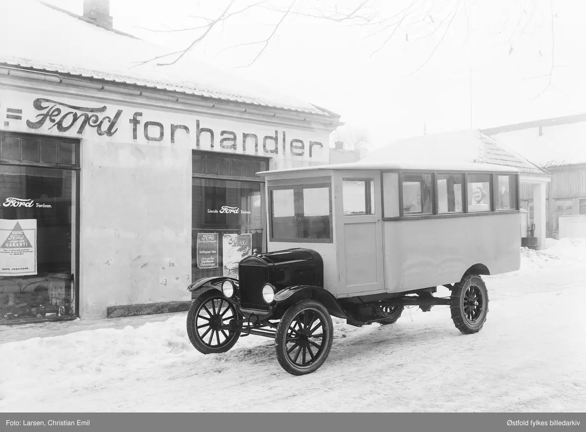 Bilforretning i Sarpsborg. Ford-forhandler. Buss av merke Ford. Ford-forhandleren i Sarpsborg het Stamsaas (og heter fortsatt det) og holdt til i Pellygata 66 i krysset Pellygata/Jernbanegata. Bilen står i Jernbanegata. På motsatt side av Pellygata var det bensinstasjon og taket over pumpene kan sees over taket på bussen. Bygget står fortsatt og huser i dag (2016) en hurtigmatkjede.

Siden det er en Ford TT, som gikk ut av produksjon i mai 1927, og den ser ut til å være flunk ny og ennå ikke registrert (leveransefoto), er bildet neppe tatt i 1929-30. Kanskje heller ikke 1928. Byggetid for bensinstasjonen, med valmtak og hjørnestolpe synlig over/bak bussen, kan avgrense mulig tid for foto ytterligere.(Ivar Stav 2016)

Reklameplakat i vindu: 
Brukt Ford selges med garanti. 
kjøp av en brukt Fordvogn er sikkerhet
Kom indenfor.