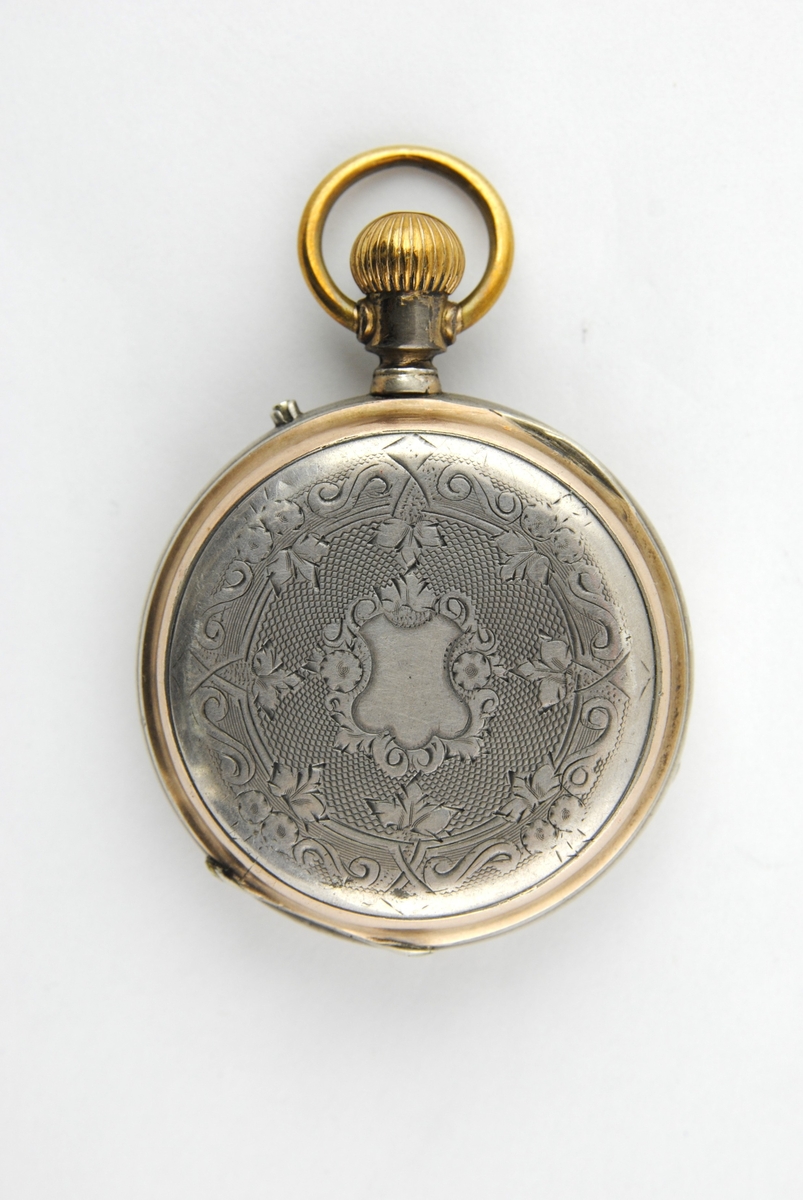 Herrmodell med förnicklat fodral. Boetten i silver och guld. Rikt graverat på baksidan. Stämplad DMF o CO på insidan locket och innanför Cylindre o Rubis. Urtavlan har romerska siffror, minutsiffror vid varje 5 minuter i arabiska siffror. Separat sekundvisare nertill. Kron uppdragning.