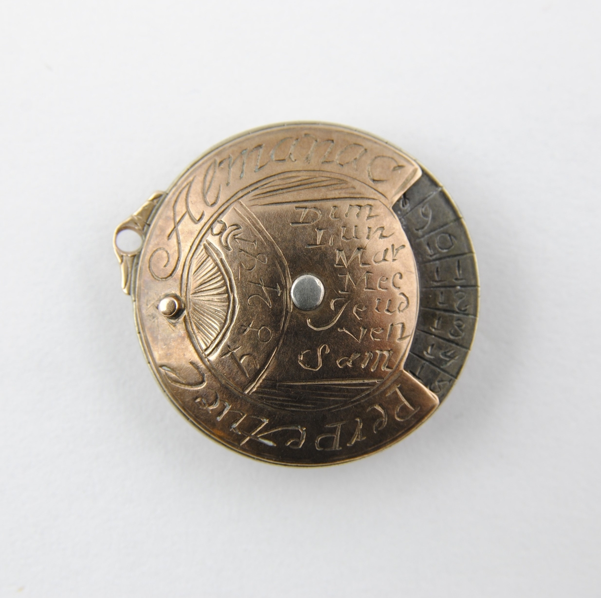 Vit och rödaktig metall, möjligen järn och koppar. Graverad på franska med månader, dagar, datum och zodiaksymboler. Gulddoublé kedja, länk och stav. 700 mm lång.