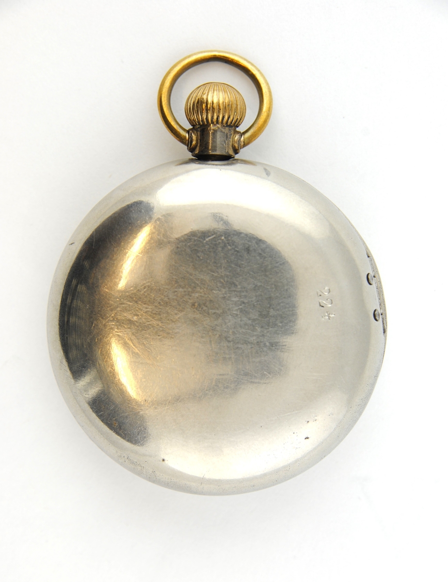 Herrmodell med förnicklat fodral. Boetten i silver och guld. Rikt graverat på baksidan. Stämplad DMF o CO på insidan locket och innanför Cylindre o Rubis. Urtavlan har romerska siffror, minutsiffror vid varje 5 minuter i arabiska siffror. Separat sekundvisare nertill. Kron uppdragning.
