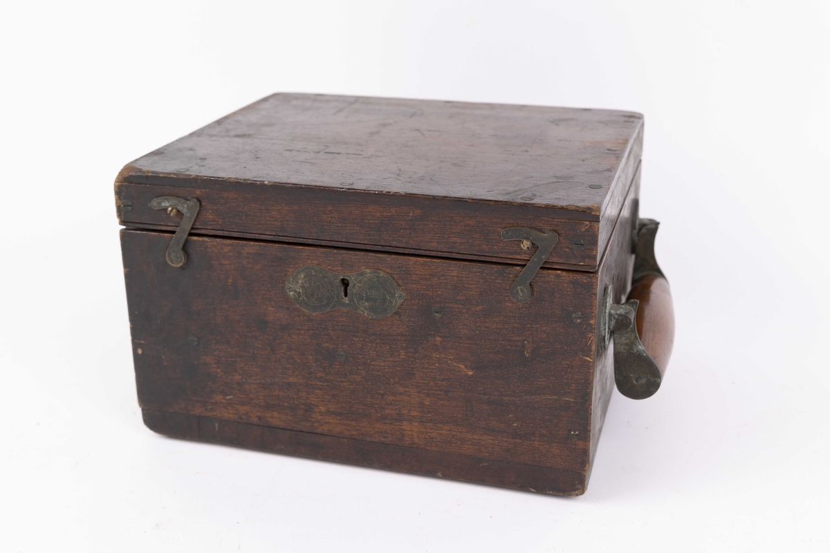 Dampmaskinindikator med flere deler i brun trekasse. Kassen har lokk med hengsler, innvendig hengslet plate til romavdeler og oppbevaringsfester for løse deler. Indikatoren er festet til ene kortsiden og vippes ut ved bruk. Instrumentet har en sylinder. 
