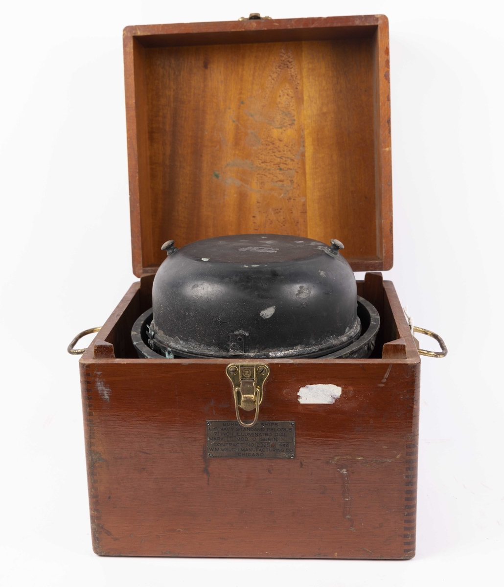 Gyrokompass med oppheng og siktedioptere, med elektrisk tilkobling og lys. Metallhette over kompasset. Oppbevart i egen transportkasse