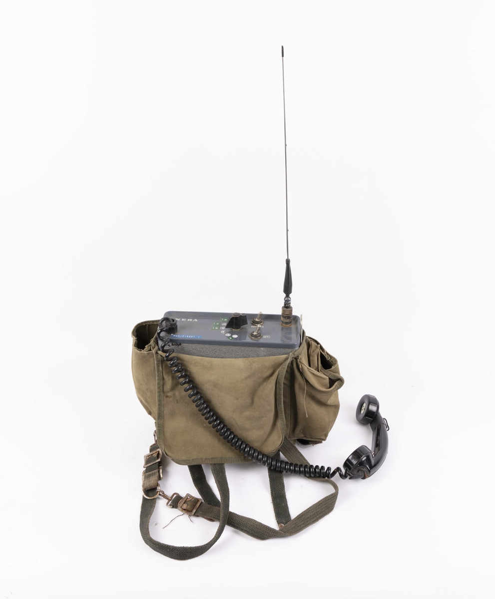 VHF-radio i tøyveske. Bærbar radiosender/mottaker i metall med antenne og telefonrør. Oppbevares i grønn tekstilveske med skulderreim.