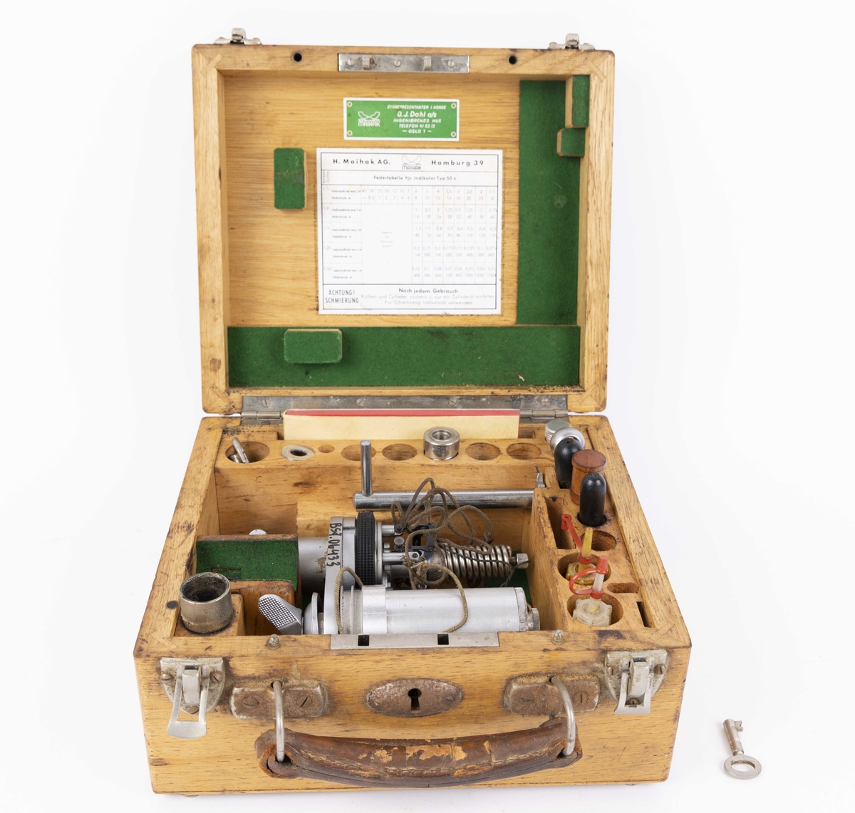 Indikator til måling av maskinhestekrefter. Dampmaskinindikator med flere deler i brun trekasse. Kassen har hengslet lokk og oppbevaringsrom for løse deler som oljeflasker, skrujern, krok, hefte med røde ark, nøkkel, linjal og andre deler. Med håndtak i skinn og lås med nøkkel.