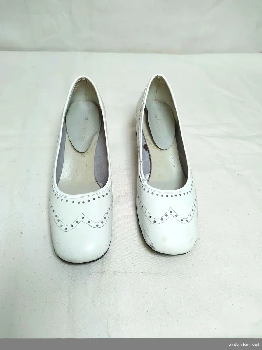 Hvite pensko til dame i skinn. Hullmønster. Noe høyde på hælene. I antatt uoriginal skoeske, da esken er har påskriften "Fine Line Romantique".