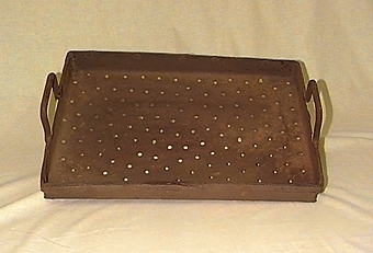 Rektangulärt metallstycke med uppvikta kanter, och sidor förstärkta med fastnitat metallband. På översidan övergår metallbandet till rektangulära handtag. Botten är perforerad med små hål.