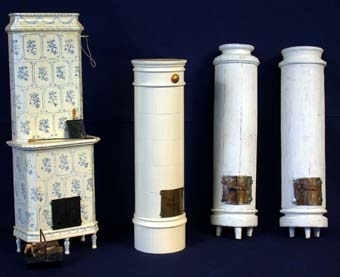 Kakelugn av vitmålat trä med lucka framtill i mässing som går att öppna och låsa med fungerande låsanordning. På ena sidan en metallkrok med garnbit som spjällsnöre. Kakelugnen rund i formen med profilerade lister och ristade kakelplattor i relief. Botten märkt: "Nolbyn" och "Värmländskt hantverk".