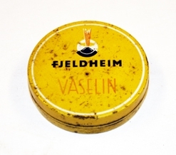 Eske med vaselin. Sirkulær. Metall. Lokket trees over bunn. Skrift og illustrasjon på lokk.