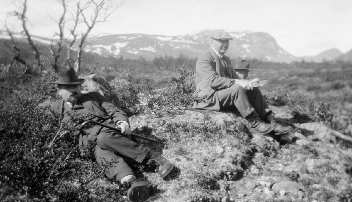Tre menn som hviler i lyngen med fjell i bakgrunnen. Bildetekst: "Widt og Morseth i Sikkilsdalen sommer 1928"