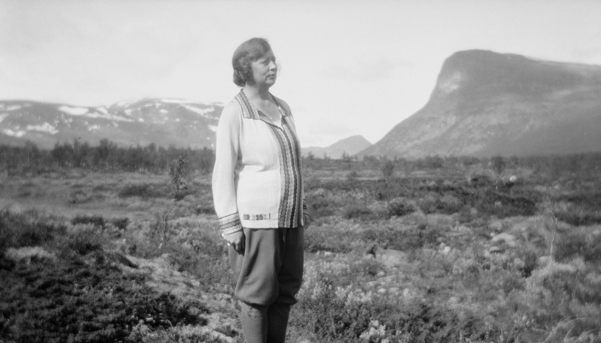 Dame i turantrekk som står i Sikkilsdalen med Sikkilsdalshornet og andre fjell i bakgrunnen