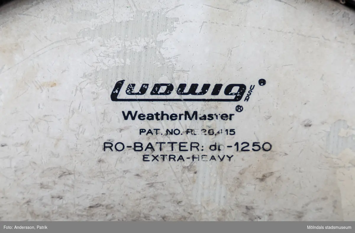 En rund trumma i metall och plastliknande material i cremefärgat pärlemoliknande mönster, samt två tillhörande avsmalnande långa trumpinnar i trä. Trumman ser ut att vara väl använd då ovansidan är missfärgadav trumslag. Trumman har ägts och spelats av Holger Åkerström. Holger var född 15/3 1904 i Örgryte.