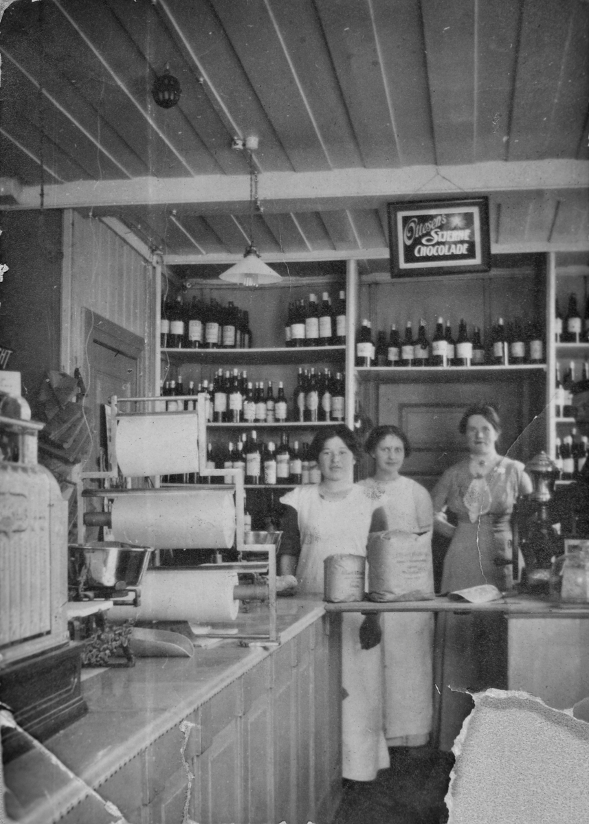 Bildet viser en av de første jødiskeide butikkene i Trondheim, en vinhandel på Nedre Bakklandet 5. Startet ca. 1900 og het Jacobsens's. På bildet er Esther Jacobsen, senere gift Bekker og Marie Dworsky, senere gift Hirsch. De tre kvinnene står bak disken med vinflasker bak seg.