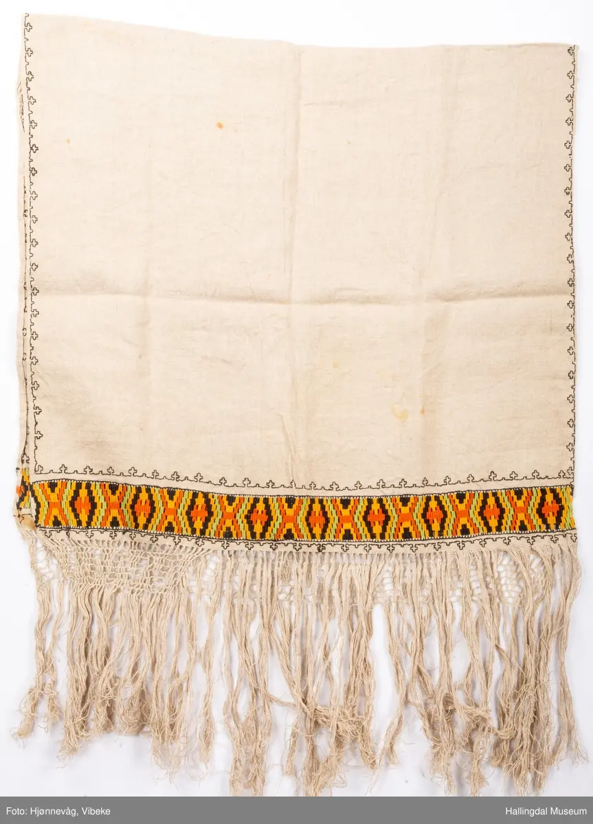 Vevd løper, toskaft i lin med frynser, beige. Broderi holbeinsøm. Nær frynsene er det broderi som ser ut som det er kelimvevd (uttrekksøm); svart, orange, sennep og grønt. Frynser med firflettet blonde i begge ender. Firflettingen er ikke gjort ferdig.