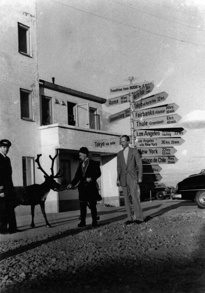 Stasjonssjef i SAS, Einar Johnsen, Karl Kalstad med et reinsdyr og leder for Winge reisebyrå, Buster Eriksen oppstilt ved veiviseren ved Bodø flyplass.