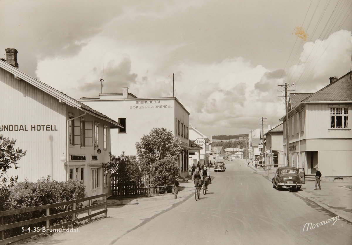 Postkort, Ringsaker, Brumunddal hotell, Furnesvegen, Brumunddal Bok og Papirhandel, Sparebanken Hedmark, Esso bensinstasjon, til høyre Samvirkelaget, folk og biler på riksveg 50, bil med registreringsnummer A-60937,