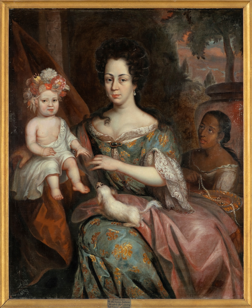 Portrett av grevinne Wilhelmine Juliane von Aldenburg (1665-1746), som var femte og yngste datter av den tyske greven Anton I von Aldenburg (1633-1680) og hans første kone Augusta Johanna von Sayn-Wittgenstein (1638-1669). Faren var danskekongens stattholder i grevskapene Oldenburg og Delmenhorst, som i perioden 1667-1773 var en del av den danske staten. Wilhelmine Juliane giftet seg i 1689 med et annet medlem av samfunnseliten, Georg Ernst Wedel Jarlsberg (1666-1717). Han var sønn av den tyske offiseren Gustav Wilhelm von Wedel (1641-1717) og Marie von Ehrenreiter zu Evenburg (1633-1702). Svigerfaren var også i danskekongens tjeneste, fra 1681 som stedfortredende kommanderende general i Norge. Wedel var en av de største kreditorene til stattholder Ulrik Fredrik Gyldenløve (1638-1704), som var greve av Larvik og Jarlsberg, og fra 1677 gift med Wilhelmine Julianes eldste søster, Antoinette Augusta (1660-1701) von Aldenburg. For å gjøre opp gjelda solgte Gyldenløve i 1683-84 det nordre grevskapet til svogeren, som dermed ble grev Gustav Wilhelm von Wedel-Jarlsberg. Wilhelmine Julianes ektemann var arving til dette grevskapet, men ettersom han døde et snaut år før faren, var det deres sønn Fredrik Anton Wedel Jarlsberg (1694-1738) som ble den neste greven. Dette portrettet skal være malt på Aldenburgernes slott i Evenburg i 1691. Barnet som sitter ved sida av Wilhelmine Juliane skal være hennes første barn, komtesse Maria Wedel-Jarlsberg (1690-1740). Datteren giftet seg som voksen med den britisk-hannoveranske Georg Hellvig Sünold riksfriherre von Schütz (d. 1740). På fanget hadde grevinnen en hund, og til høyre i bakgrunnen skimter vi en mørkhudet kvinnelig tjener som vi dessverre mangler informasjon om. Vi kjenner ikke identiteten til kunstneren. Bildet henger på Jarlsberg hovedgård.