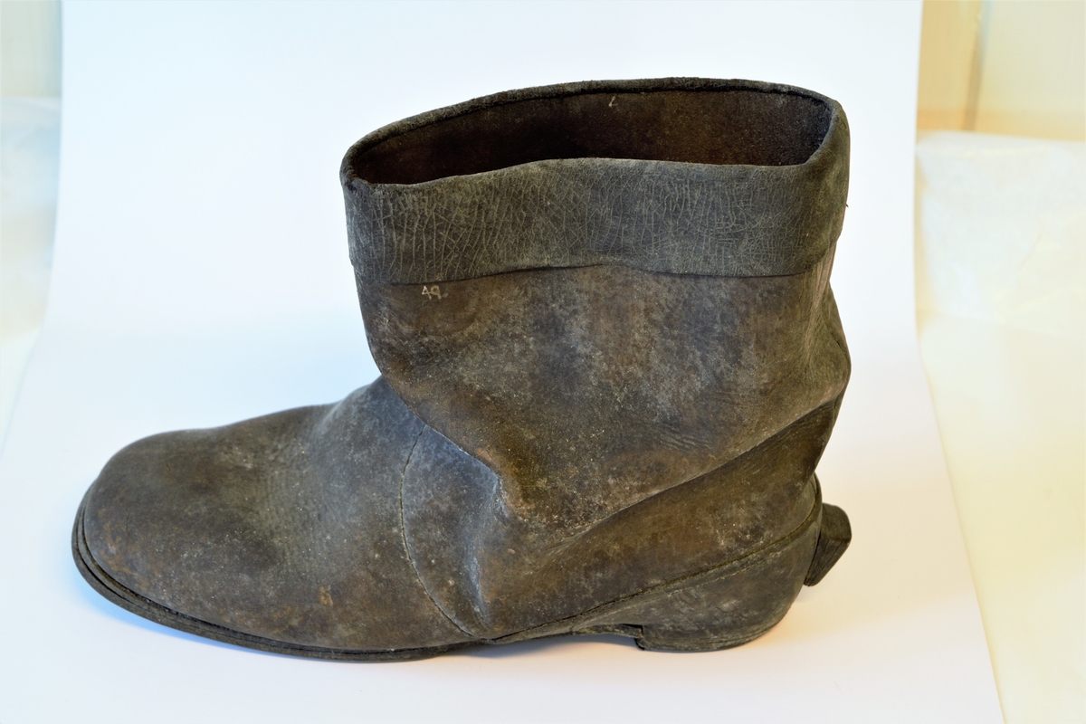 Lav lærstøvel til mann. Såle og hæl av flere lag lær. Øvre del sydd av tre lærstykker, dobbeltbrettet 4 cm bred kant øverst.