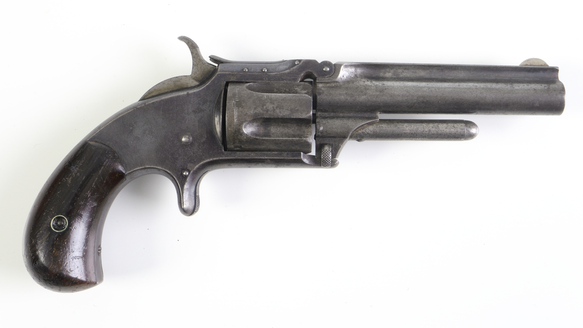 Revolver, Smith & Wesson, med trumma kamrad för fem patroner och räfflad pipa. Revolvern är enkelverkande, d.v.s. man måste spänna hanen manuellt innan skott kan avlossas. Plunderstock finns fast monterad under pipan, något som gör att man måste fälla upp pipan genom att lossa en spärr strax under trummans främre del, s.k. tip-up model. Därefter kan man, efter borttagande av trumman, trycka ut tomhylsorna. Sidoblecket är blånerat, och revolvern har en rundad kolv med kolvplattor av trä. Riktmedlen är fasta.
Inskrivet i huvudkatalogen 1971.