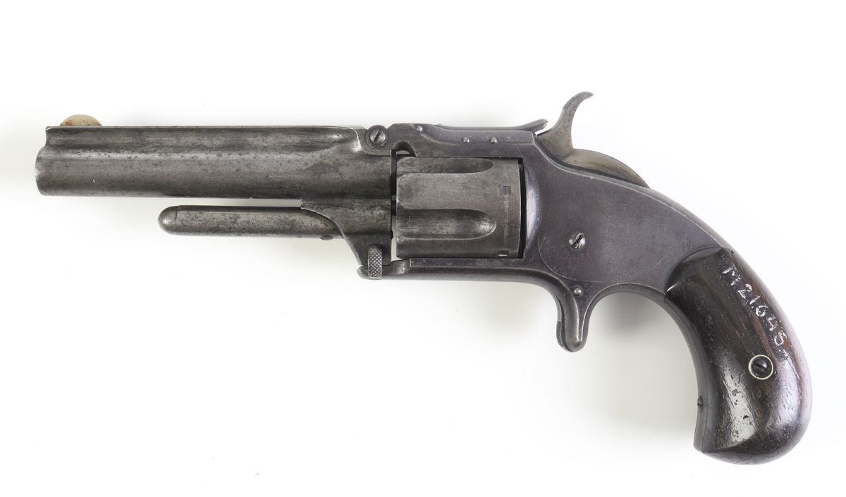 Revolver, Smith & Wesson, med trumma kamrad för fem patroner och räfflad pipa. Revolvern är enkelverkande, d.v.s. man måste spänna hanen manuellt innan skott kan avlossas. Plunderstock finns fast monterad under pipan, något som gör att man måste fälla upp pipan genom att lossa en spärr strax under trummans främre del, s.k. tip-up model. Därefter kan man, efter borttagande av trumman, trycka ut tomhylsorna. Sidoblecket är blånerat, och revolvern har en rundad kolv med kolvplattor av trä. Riktmedlen är fasta.
Inskrivet i huvudkatalogen 1971.