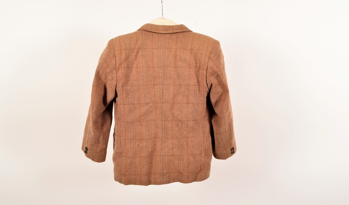 Dressjakke til gutt, mest sannsynlig i ullstoff. Mellombrun farge med vevde innslag av rødbrunt og mørkebrunt,  i tynne striper som utgjør et rutemønster. Tilhørende kortbukse og sokker/strømper har arkivnummer VFF 20771 og VFF 20772.