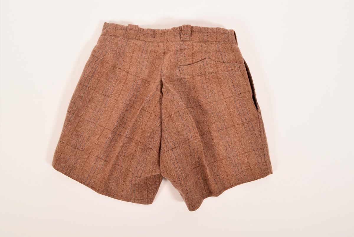 Dressbukse til gutt, mest sannsynlig i ullstoff. Mellombrun farge med vevde innslag av rødbrunt og mørkebrunt,  i tynne striper som utgjør et rutemønster. Baklomme på høgre side. Fôr i linningen og knapper for bukseseler på innsiden Tilhørende dressjakke og sokker/strømper har arkivnummer VFF 20770 og VFF 20772.