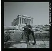 2795 Grekland Akropolis. Fotograf med kamera på stativ framför runierna av templet Parthenon.