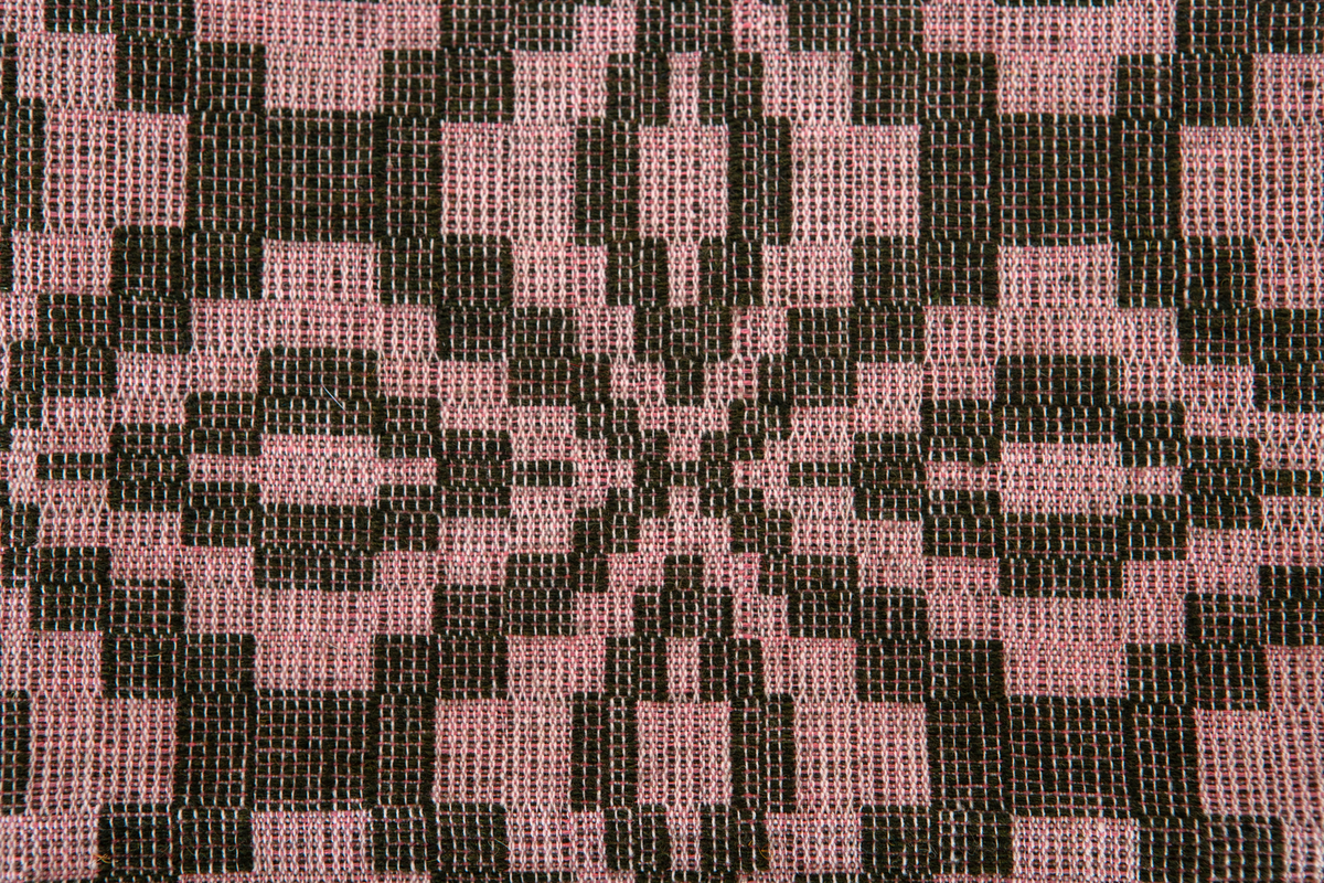 Möbeltygsprov vävt i jämtlandsdräll med oblekt bomullsgarn i varpen och grönt ullgarn i mönsterinslaget, rosa bomullsgarn  som mellaninslag.Provet har en påsydd bomullslapp med handskriven text: Bollnäs Hemslöjdsförening 79.En maskinskriven papperslapp med texten: Möbeltyg i jämtlandsdräll B.G 1920-talet är fästad vid provet.