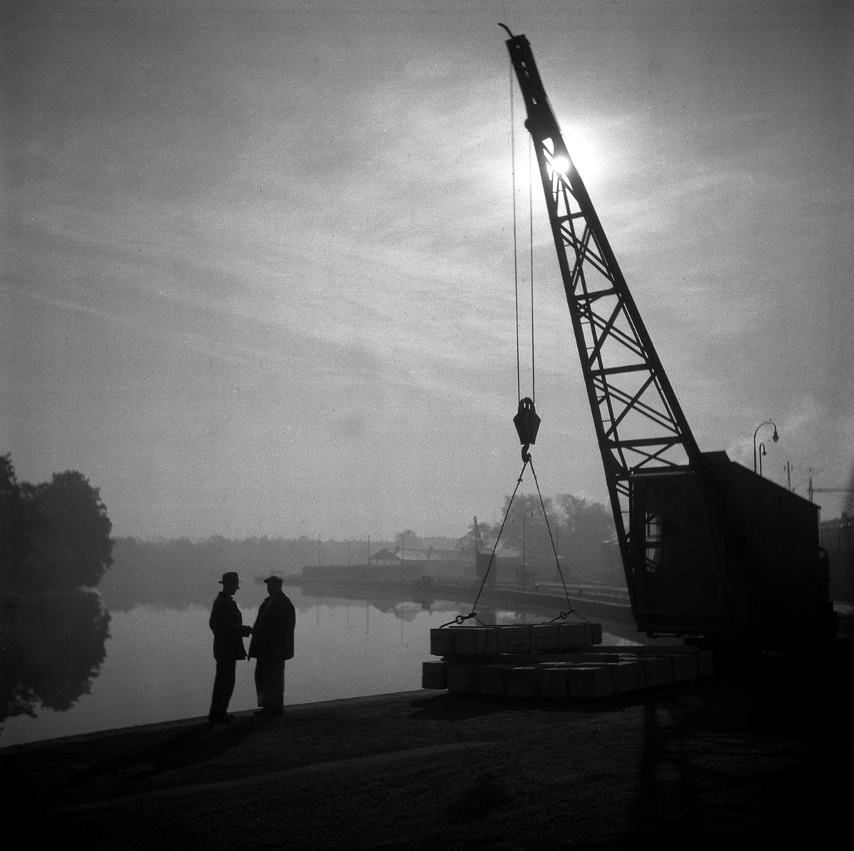 Linköpings hamn en disig dag 1949. Tanken på en väl tilltagen hamn i slättstaden Linköping väcktes när planerna av Göta kanal sköt fart i början av 1800-talet. Stångån muddrades och en rad byggnadsprojekt kring hamnen realiserades. Sjöfarten kom att få stor betydelse för staden, än större efter Kinda kanals tillkomst och stadens uppgradering till stapelstad under 1870-talet. Med väg- och spårtransporternas ökning kom hamnens betydelse att minska. I mitten av förra seklet kunde man som vår fotograf söka stillhet på platsen.