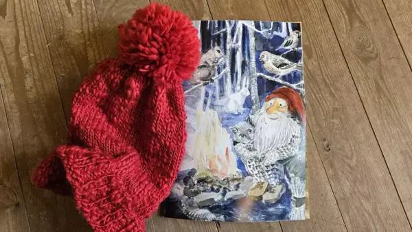 Foto av nisselue og postkort med nisse som sitter ved et bål.