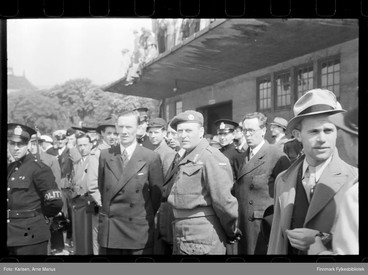 En gruppe tilskuere venter på regjeringens ankomst til Oslo den 31. mai 1945

Kronsprins Olav V som nr. 3 fra høyre. Til venstre for kronsprinsen står Oscar Torp og til høyre, Terje Wold 

En mann i politi uniform står bak kronprinsen og én til helt til venstre

Skipet Andes anløp Oslo Havn med eksilnordmenn fra regjering og administrasjon

Notat tilhørende negativene beskriver serien (fbib.93091-001- 034) som: Regjeringen og Kong Haakons ankomst til Oslo 1945. Ser statsminister Nygaardsvold på landgangen samt Haakon Olav og Scharffenberg på talerstolen