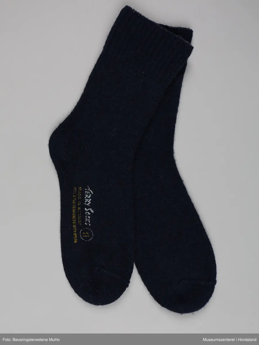 Eit par marineblå strikka ullsokkar frå Samnanger fabrikker i str. 11. Den eine sokken har tekst trykt på under foten: "Terry socks, made in Norway, reinforced with nylon, 11". sokkane har vore festa saman med ein papimerkelapp med ein skiløpar på, og teksten "Safa sport - sterk og varm".