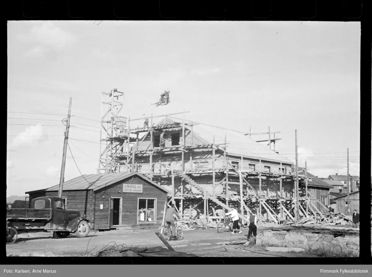 Bygg konstrueres i Kirkenes etter krigen. Ved siden av står et mindre hus med skilt "O. M. Hatle & Co."