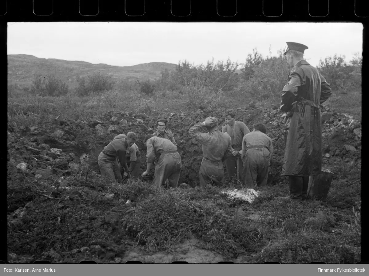 Stor fellesgrav for russere i nærheten av Kirkenes etter krigen. En politimann står til høyre og observerer. Flere unge menn i uniformer arbeider med å grave opp lik.

Foto trolig tatt på slutten av 1940-tallet, tidlig 1950-tallet