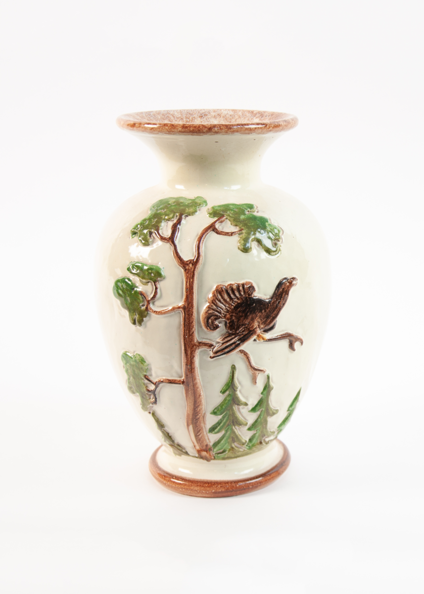 Dreid urneformet vase med stor vid krage på fotring. Gul bunnglasur med brun kant og brun innside i kragen. Skogsmotiv med gran og furutrær og tiur/orrfugl.