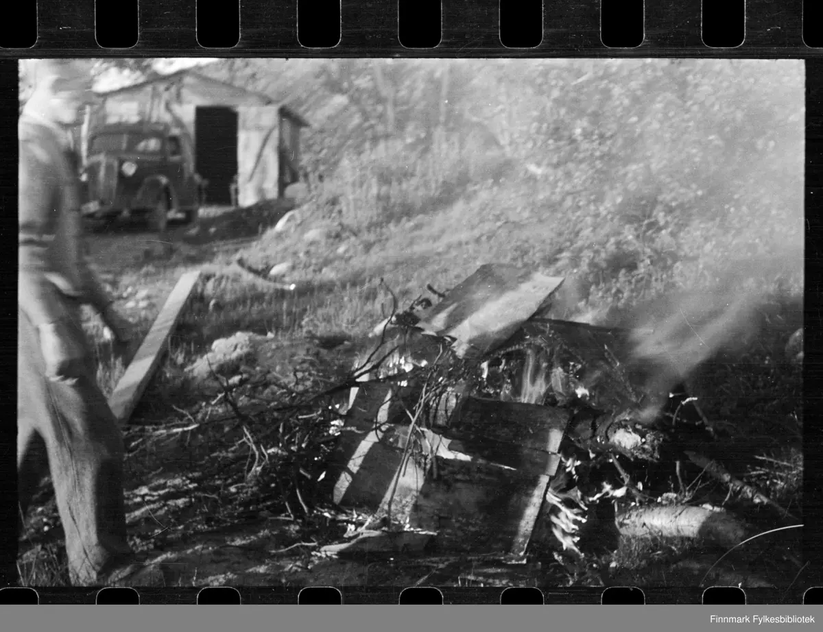 Foto av bål, antagelig i Kirkenes

I bakgrunnen kan man sen et bygg og en bil

Ved siden av bålet står en mann 

Foto trolig tatt på slutten av 1940-tallet, eller tidlig 1950-tallet