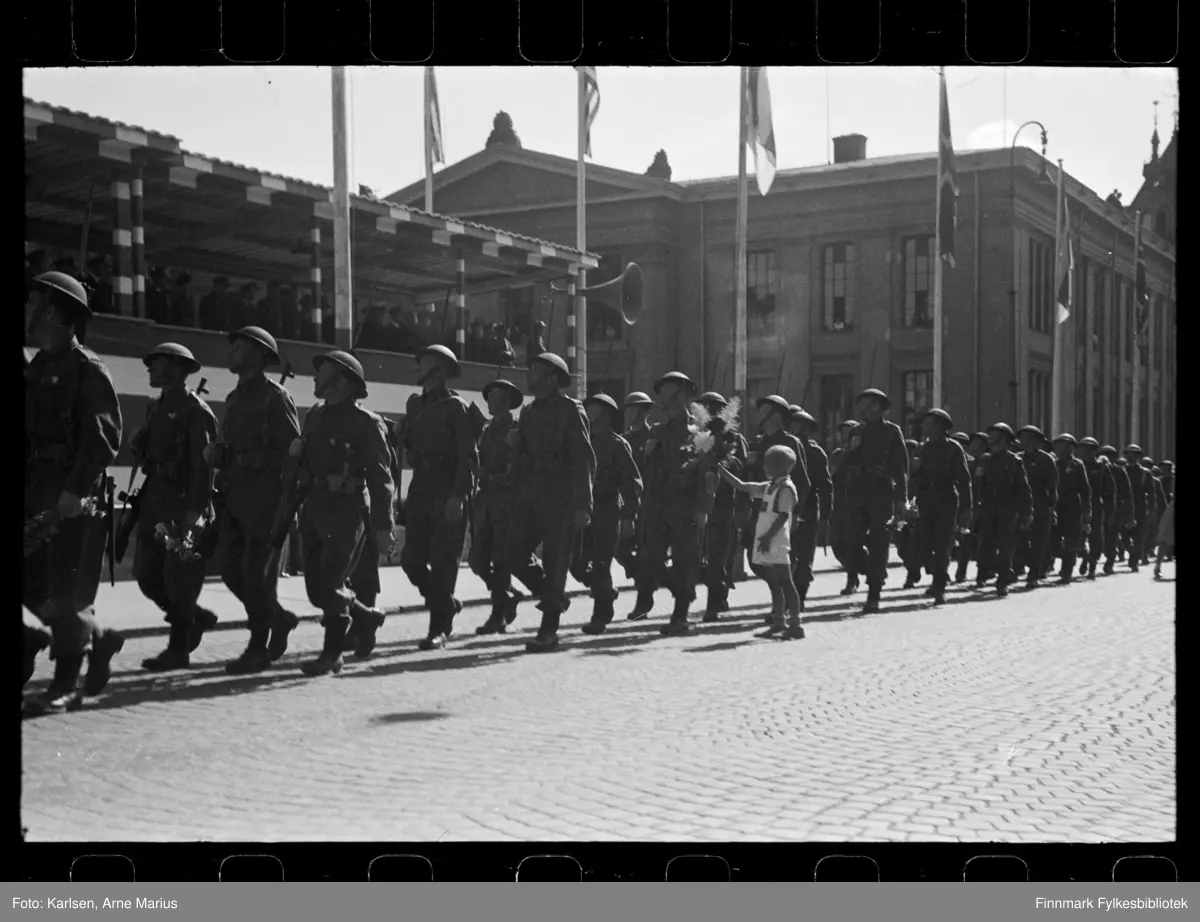 Britiske soldater marsjerer i parade på de alliertes dag den 30. juni 1945 (The Allied Forces day)

En gutt rekker en soldat blomster i det paraden går forbi 

I bakgrunnen kan man se en tribune der flere offiserer står å ser på paraden. Tribunen var satt opp foran Universitetsplassen på Karl Johan 