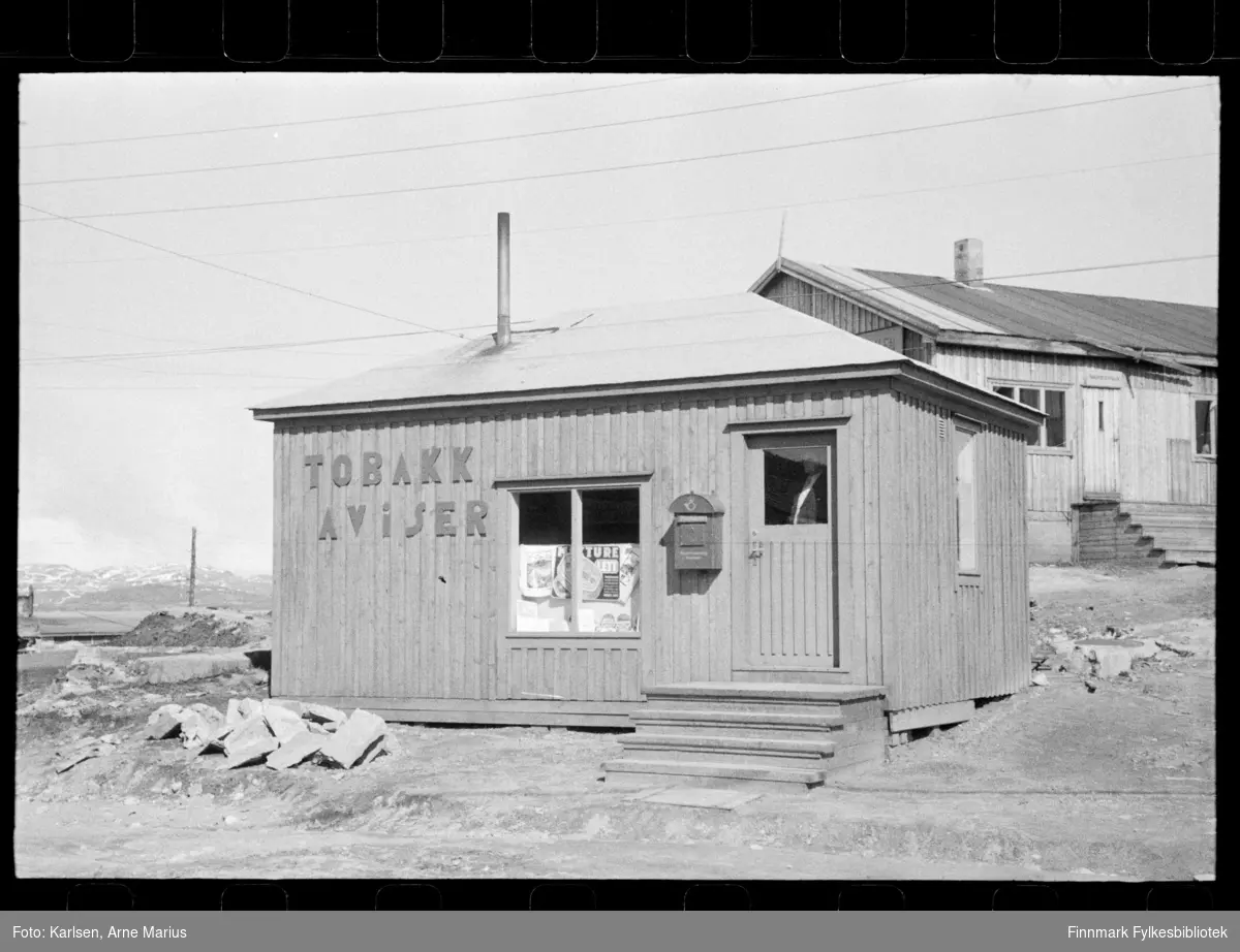 Kiosk i Kirkenes rett etter krigen

På veggen står teksten: Tobakk, Aviser 

Man kan også se en postkasse hengende ved siden av inngangsdøren 

Foto trolig tatt på slutten av 1940-tallet, tidlig 1950-tallet