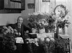 Porträtt. Man sittandes vid blomsterbord.