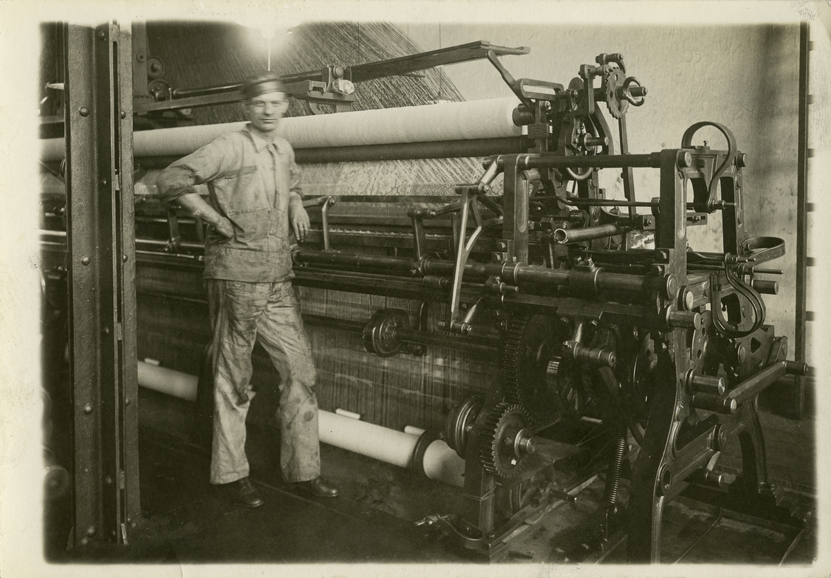 Arbeidar ved maskin, truleg ved Skandinaviska Trådgarnfabriken i Stockholm. Fabrikken var ei underavdeling av Skandinavisk Aktie Tyllgarnfabrik (seinare Tangens Gardinfabrikk) i Bergen mellom 1898 og 1920-talet.