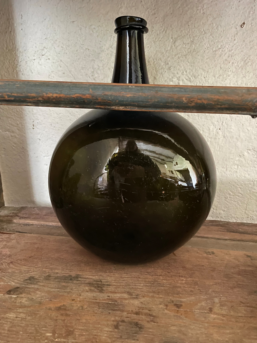 Flaska pôttepôtt av grönt glas, klotformad tillplattad bål och kort hals.