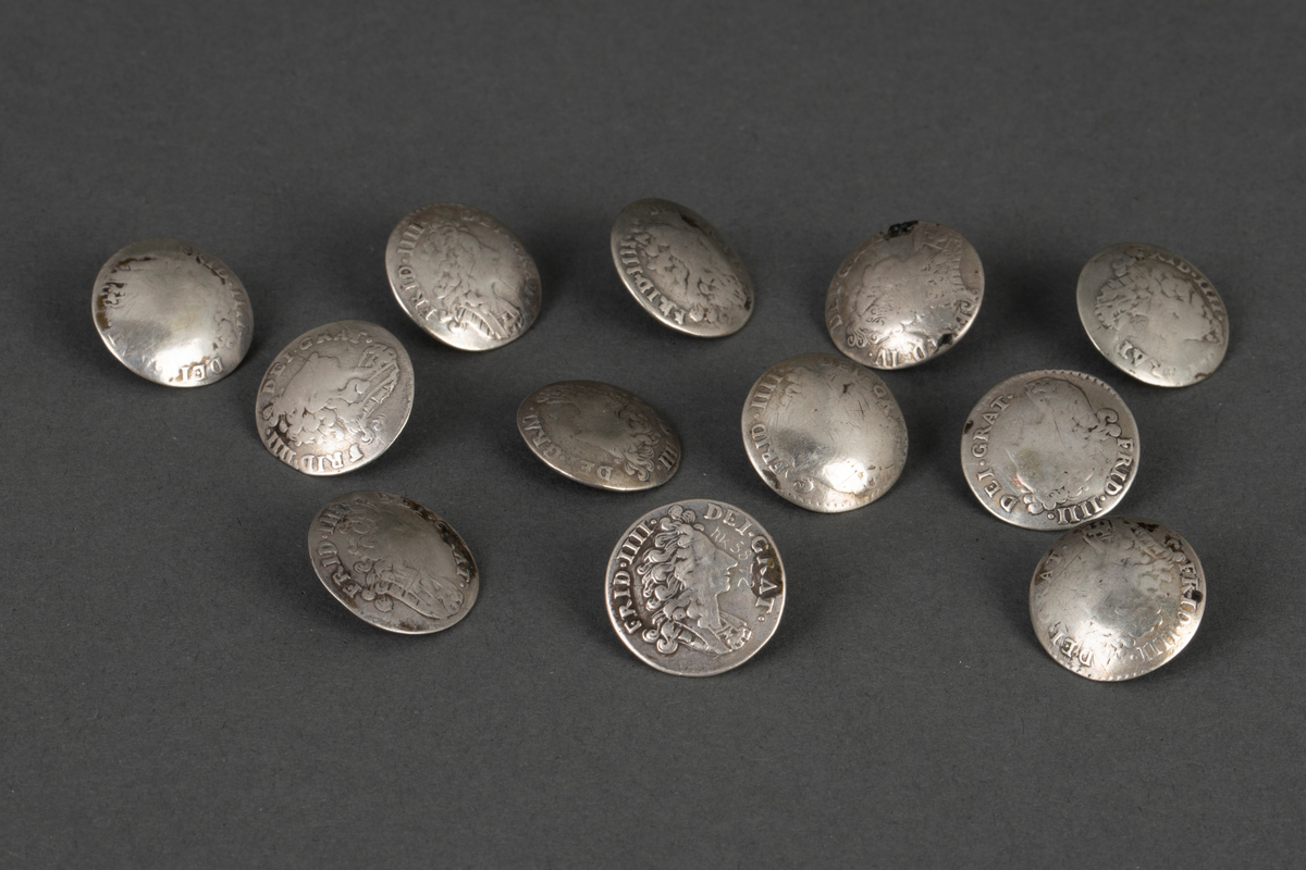 Tolv like støpte knapper i sølv. Knappene er runde, lavt hvelvede og har en fast bøyle på baksiden. På forsiden i relieff: kongeportrett i profil og omskrift "FRID. IIII: (på én knapp FRID IV) DEI. GRANT. På baksiden: Krone og omskrift "DAN. NOR. VAN. GOT. REX., samt 8 S, D. M. A." og forskjellige årstall "1702, 1703 (to ganger), 1704 (to ganger), 1705, 1707, 1709, 1712, 1713 (to ganger), og 1714". Knappene er laget av mynter (8 skilling).