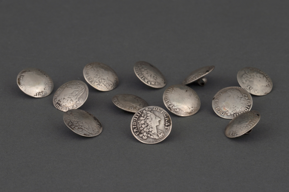 Tolv like støpte knapper i sølv. Knappene er runde, lavt hvelvede og har en fast bøyle på baksiden. På forsiden i relieff: kongeportrett i profil og omskrift "FRID. IIII: (på én knapp FRID IV) DEI. GRANT. På baksiden: Krone og omskrift "DAN. NOR. VAN. GOT. REX., samt 8 S, D. M. A." og forskjellige årstall "1702, 1703 (to ganger), 1704 (to ganger), 1705, 1707, 1709, 1712, 1713 (to ganger), og 1714". Knappene er laget av mynter (8 skilling).