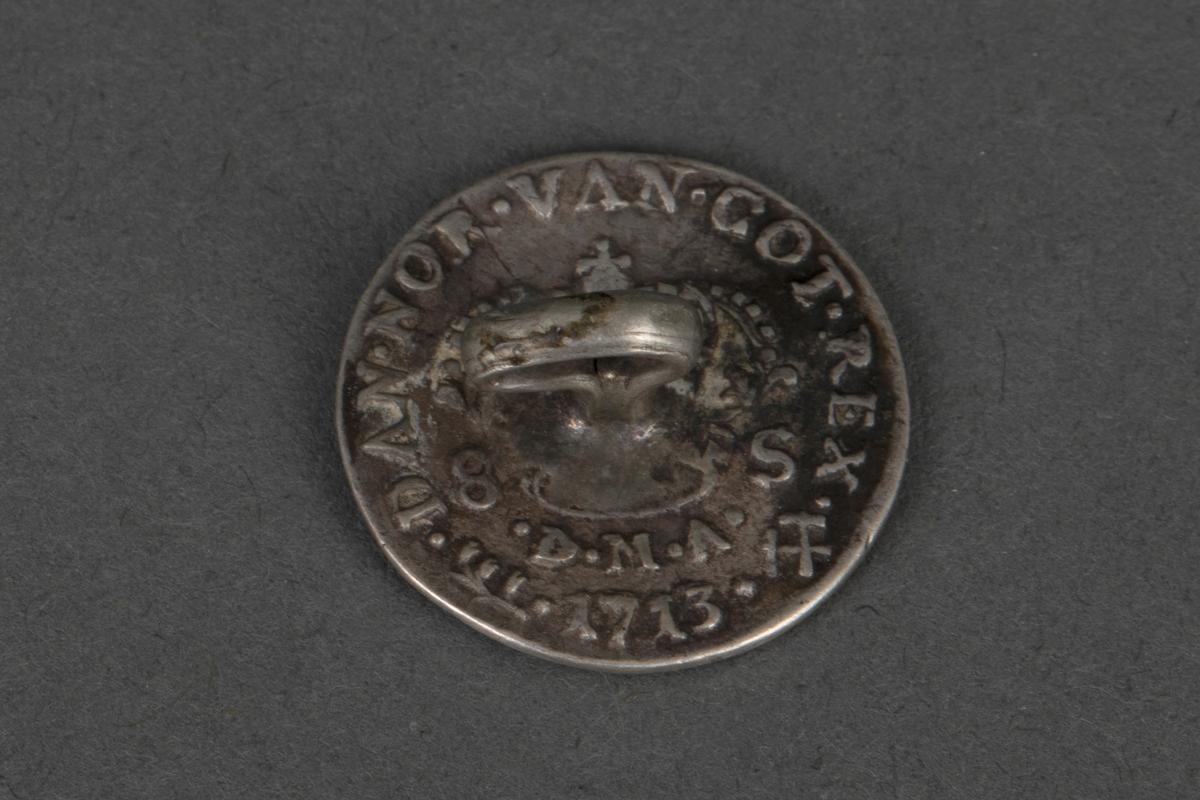 Tolv like støpte knapper i sølv. Knappene er runde, lavt hvelvede og har en fast bøyle på baksiden. På forsiden i relieff: kongeportrett i profil og omskrift "FRID. IIII: (på én knapp FRID IV) DEI. GRANT. På baksiden: Krone og omskrift "DAN. NOR. VAN. GOT. REX., samt 8 S, D. M. A." og forskjellige årstall "1702, 1703 (to ganger), 1704 (to ganger), 1705, 1707, 1709, 1712, 1713 (to ganger), og 1714". Knappene er laget av mynter (8 skilling).