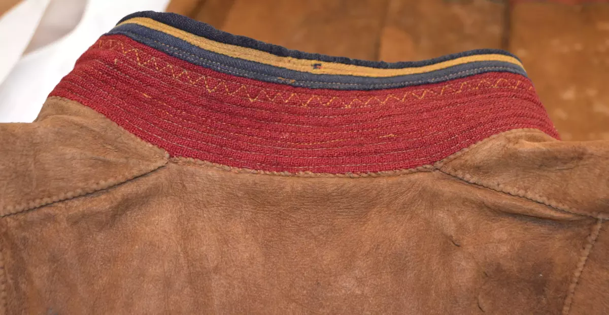 Sválltjá/kinnkofte med tekstilapplikasjoner og grindvevd pyntebånd. Goahkka/Krage i vinrød bunnfarge, uten divlle, men dekor øverst i grønt og gult. Badjelbuttas i goahkka/krage er mørkeblå. Åhtså med sájá i rødt og blått. Sase/ermedekor med sájá i blått og rødt og med badjelbuttas i brunt skinn. Nederst påsydd snjisjkodum/vevd lissto/kantband.