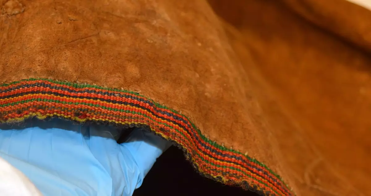 Sválltjá/kinnkofte med tekstilapplikasjoner og grindvevd pyntebånd. Goahkka/Krage i vinrød bunnfarge, uten divlle, men dekor øverst i grønt og gult. Badjelbuttas i goahkka/krage er mørkeblå. Åhtså med sájá i rødt og blått. Sase/ermedekor med sájá i blått og rødt og med badjelbuttas i brunt skinn. Nederst påsydd snjisjkodum/vevd lissto/kantband.