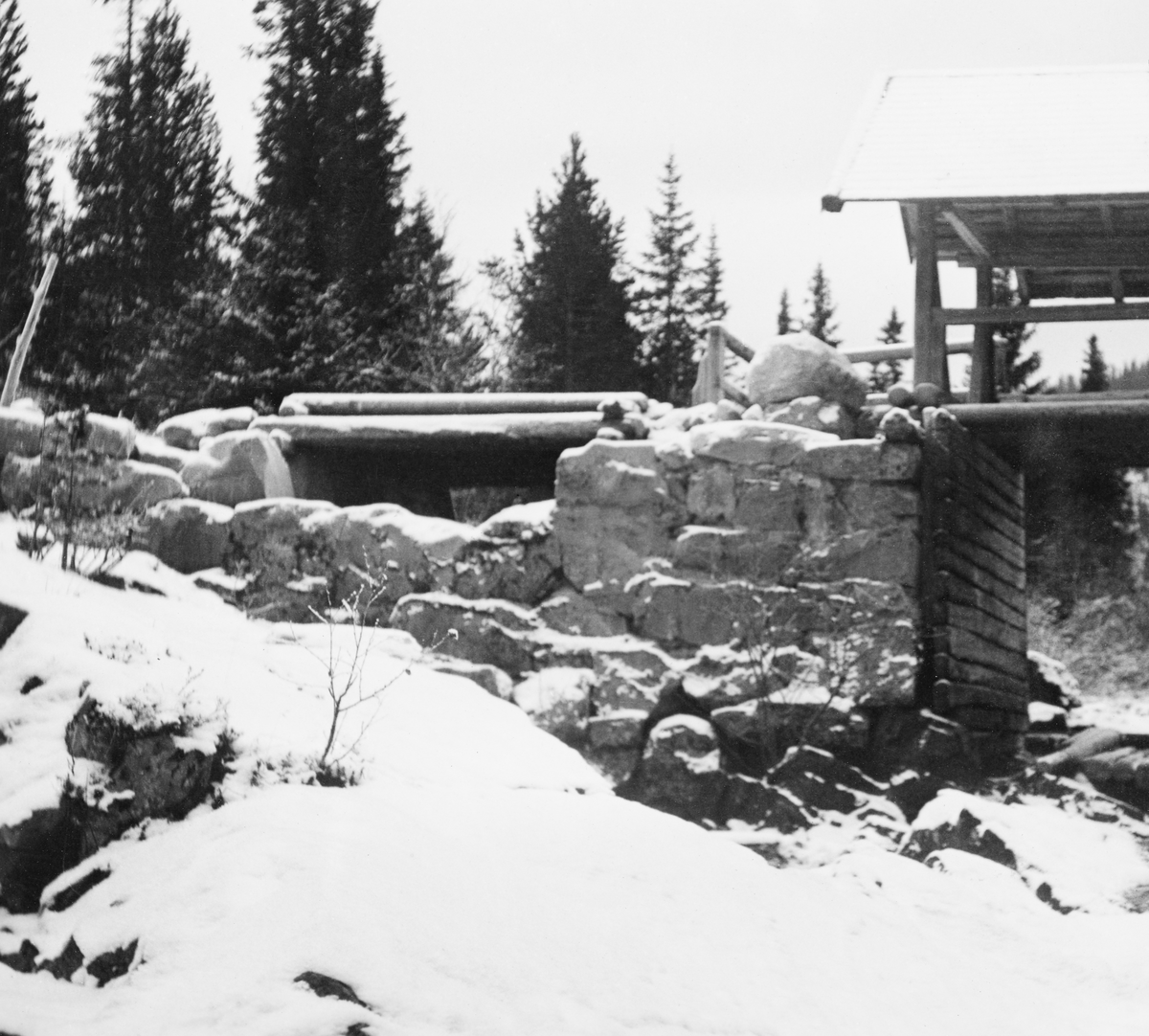 Fra Imsdammen i elva Imsa i Imsdalen, en såkalt attholdsdam like nedenfor utløpet av Søre Imssjøen, som ligger i Ringebu kommune i Oppland. Dette bildet viser anlegget slik det så ut i 1939. Til høyre i bildet ser vi deler av hovedløpet, som hadde natursteinsmurte sidevanger med tømmerforblendinger på sidene, trebru over og et saltak over den igjen som skulle beskytte underliggende trekostruksjoner mot regn og snø. Til venstre for den overbygde delen av dammen er det et en litt grunnere åpning i den murte damarmen, også den med trebru over, men her var det ikke noe tak. Dette må sannsynligvis har vært et slags overløp som trådte i funksjon hvis dammen ble vel full av vann. I Glomma fellesfløtingsgforenings album er dette bildet venstre del av en panoramamontasje, der SJF.1989-03523 er høyre del.