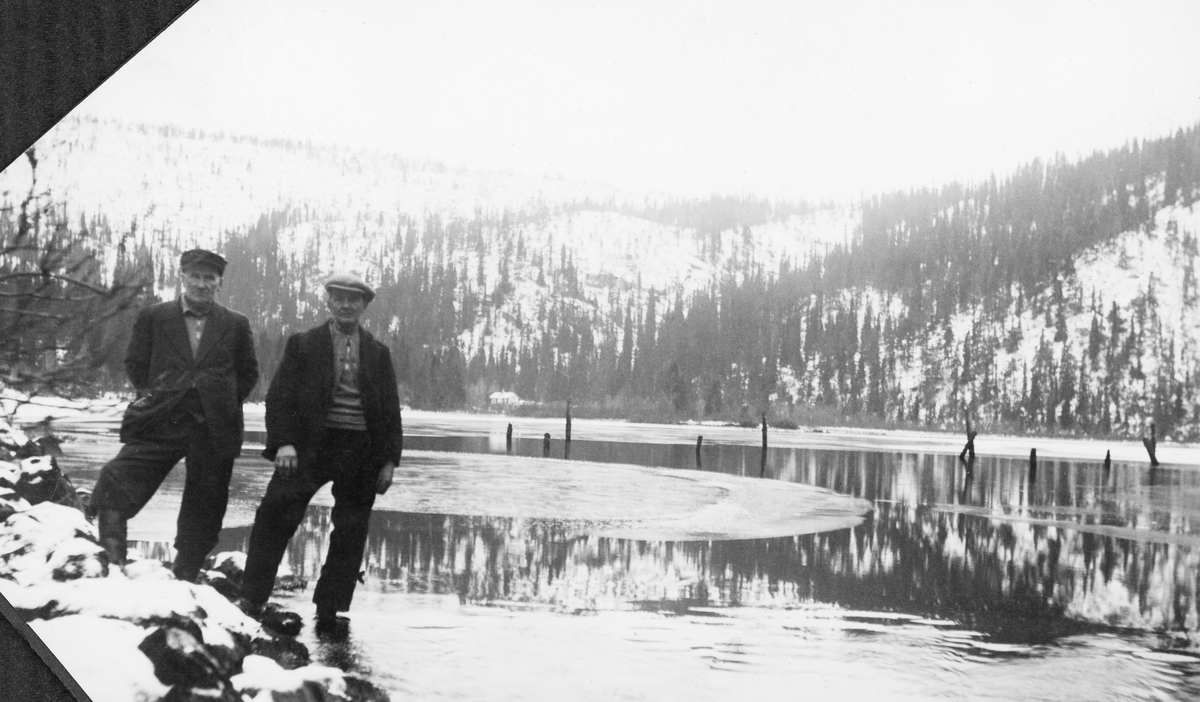 To godt voksne menn poserer for fotografen ved Søre Imssjøen, lengst øst i Ringebu kommune en kald høst- eller vårdag i 1939. Søre Imssjøen ligger 616 meter over havet og har et vannspeil med snaut en halv kvadratkilometers grunnflate. Fra nordenden av denne sjøen er det en 200-300 meter lang elvestrekning til Nordre Imsjø, som ligger om lag tre meter høyere og har mer enn dobbelt så stort vannspeil, Fløtinga på Imsa startet vanligvis ved Imsdammen, men enkelte år skal det også blitt fløtet på de to sjøene. I vannet bak de to mennene ser vi ei rekke av påler - duc d'amber - som var anleggspunkter for ei lense som antakelig ble brukt til å samle det tømmeret som etter hvert skulle fløtes nedover Imsa. I bakgrunnen, i vika i sørenden av sjøen, skimter vi Tujordsbua. I de snødekte liene ned mot sjøen vokste det glissen granskog. I Glomma fellesfløtingsgforenings album er dette bildet venstre del av en panoramamontasje, der SJF.1989-03525 er høyre del.