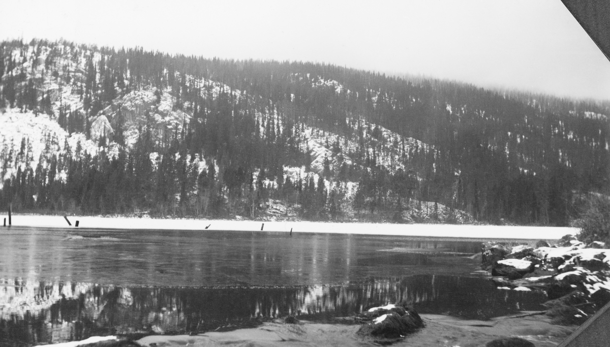 Fra Søre Imssjøen, lengst øst i Ringebu kommune, en kald høst- eller vårdag i 1939. Søre Imssjøen ligger 616 meter over havet og har et vannspeil med snaut en halv kvadratkilometer. Fra nordenden av denne sjøen er det en 200-300 meter lang elvestrekning til Nordre Imsjø, som ligger om lag tre meter høyere og har mer enn dobbelt så stort vannspeil, Fløtinga på Imsa startet vanligvis ved Imsdammen, men enkelte år skal det også blitt fløtet på de to sjøene.  Ute på den delvis islagte vannflata ser vi ei rekke av påler - duc d'alber - som var anleggspunkter for ei lense som ble brukt til å samle det tømmeret som etter hvert skulle fløtes nedover Imsa. I de snødekte liene ned mot sjøen vokste det glissen granskog. I Glomma fellesfløtingsgforenings album er dette bildet høyre del av en panoramamontasje, der SJF.1989-03524 er venstre del.
